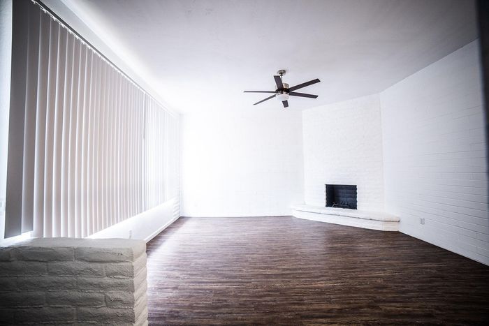 Bright, airy living room with sleek wood flooring, modern ceiling fan, and a charming white brick fireplace.