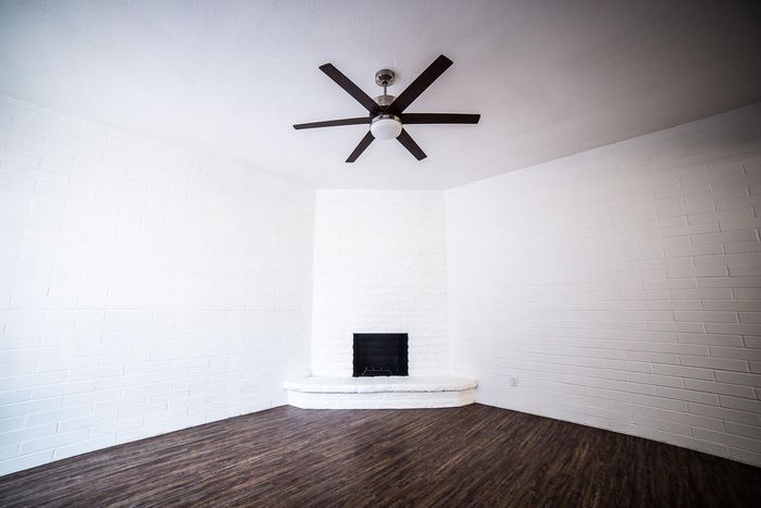 Bright, minimalist living space with a modern ceiling fan and elegant white brick fireplace, complemented by rich wood flooring.