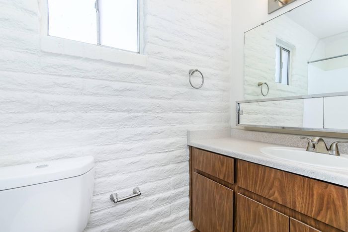 Chic modern bathroom with sleek white brick walls, elegant wood cabinetry, and a large mirror enhancing the space.