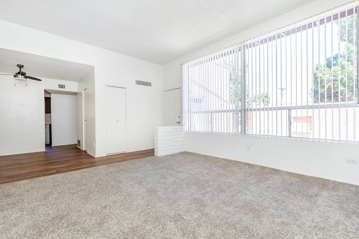 Bright and inviting living room featuring large windows with vertical blinds, plush carpeting, and modern ceiling fan.