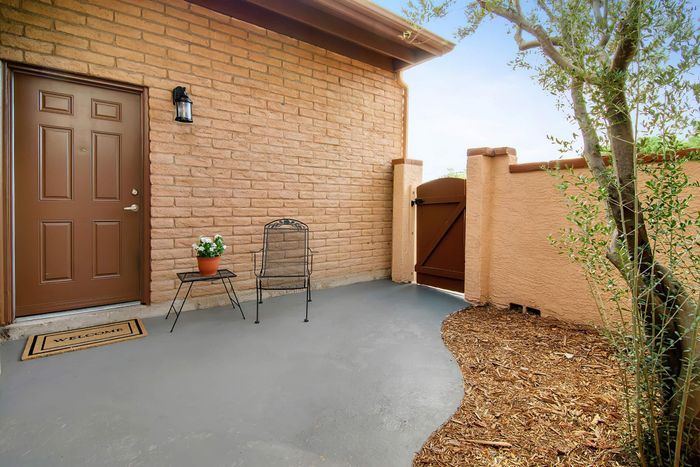 Charming front patio with a welcoming entrance, featuring a stylish metal chair, potted plant, and rustic gate.
