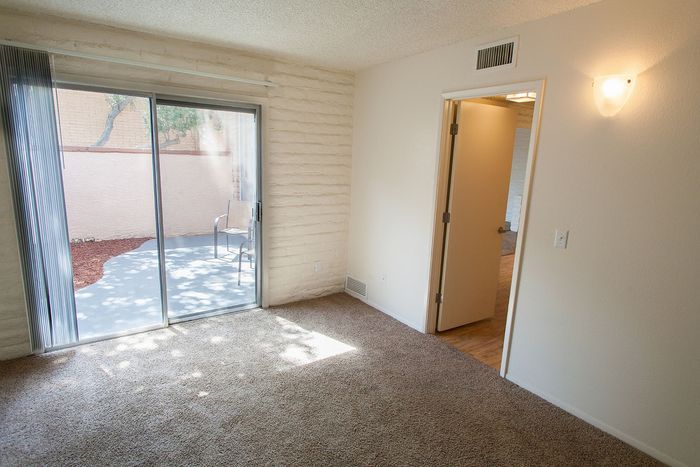 Bright room with sliding glass doors leading to a private patio, featuring neutral carpet and modern wall lighting.