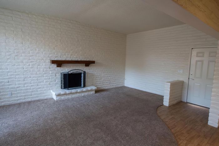 Charming living room featuring a cozy fireplace, elegant white brick walls, and soft carpet flooring.