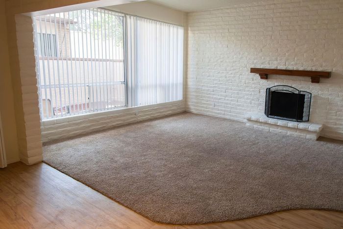 Bright living room with rustic white brick walls, large window, cozy carpet, and elegant fireplace.
