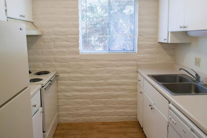 Bright, cozy kitchen featuring modern white cabinetry, double sink, and wood flooring with natural light streaming through a window.