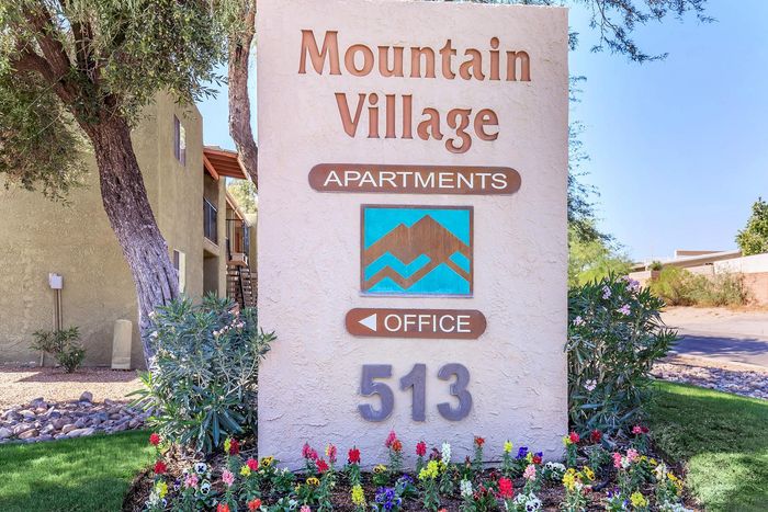 Inviting entry sign for Mountain Village Apartments surrounded by vibrant flowers and lush greenery.