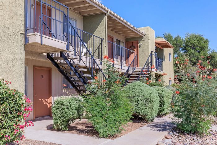 Charming apartment exterior with lush landscaping, vibrant flowers, and inviting staircases leading to modern units.