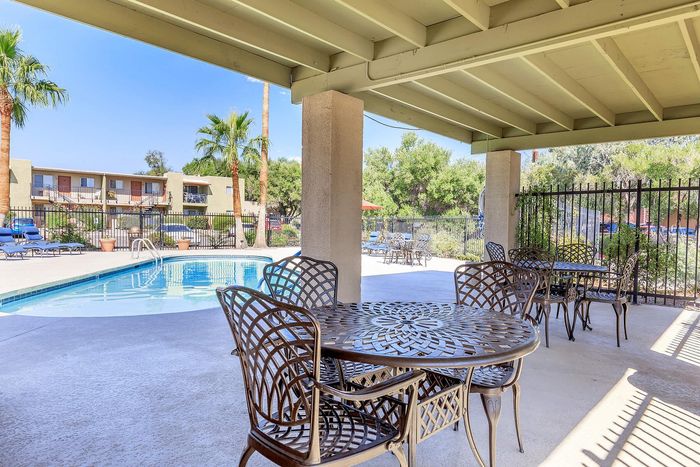Inviting outdoor pool area with stylish metal patio furniture under a shaded pergola, surrounded by palm trees and lush greenery.