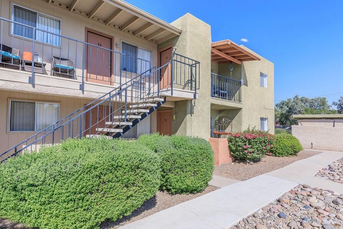 Charming apartment exterior featuring modern balconies, inviting staircases, and lush green landscaping under a bright blue sky.