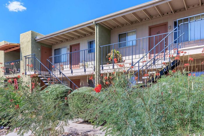 Charming apartment exterior with lush greenery and vibrant red flowers, featuring stylish railings and welcoming entrances.