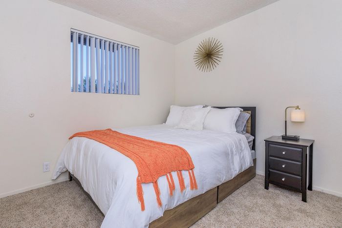 Inviting bedroom with plush bed, vibrant orange throw, and sleek nightstand in a cozy, well-lit space.