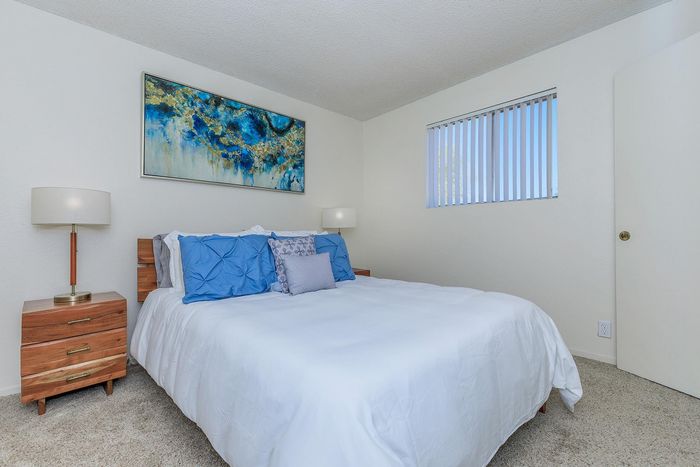 Inviting bedroom with a cozy white bed, accented by vibrant blue pillows and elegant wooden furniture, perfect for relaxation.