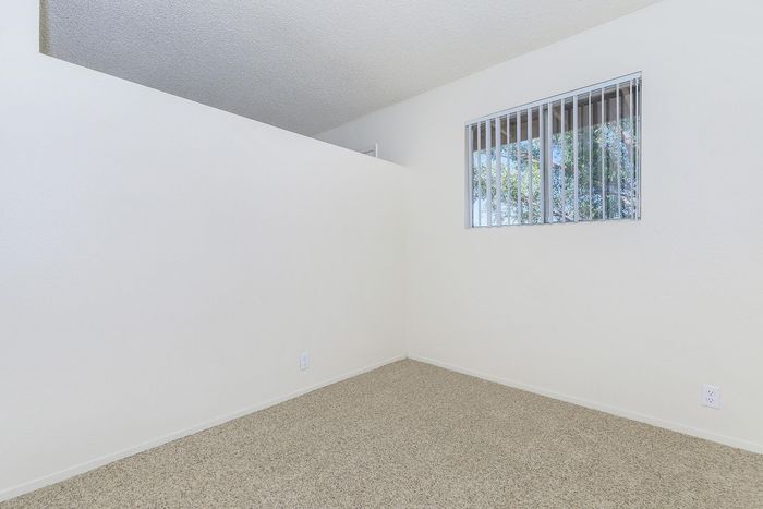 Bright and inviting bedroom with natural light, featuring soft carpeting and a large window with views of greenery.