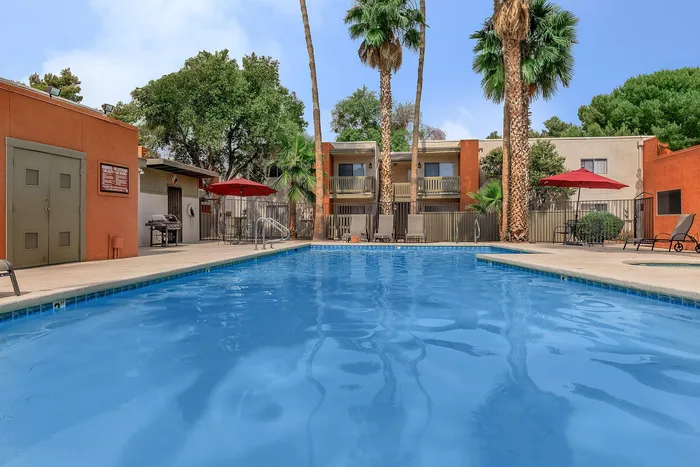 Inviting outdoor pool area surrounded by palm trees and vibrant buildings, featuring lounge chairs and red umbrellas, ideal for relaxation.