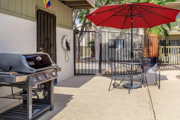 Inviting outdoor patio featuring a stylish barbecue grill, cozy seating under a vibrant red umbrella, and a secure gated entrance.