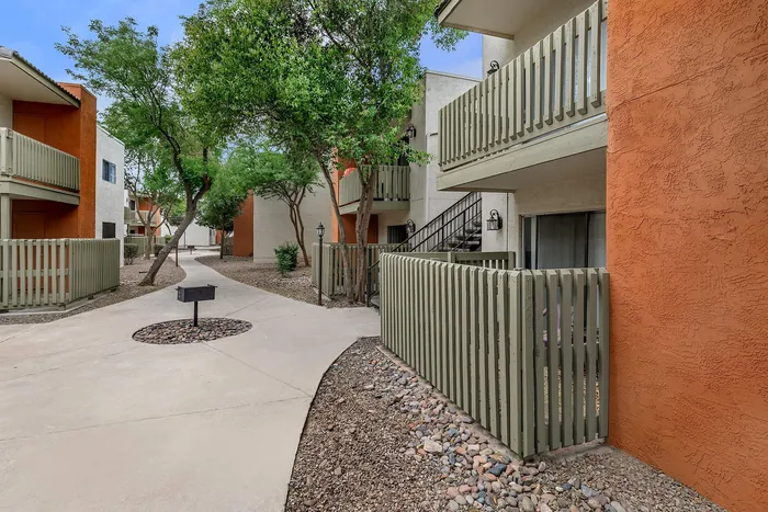 Charming apartment exterior featuring vibrant orange accents, lush trees, and inviting walkways.