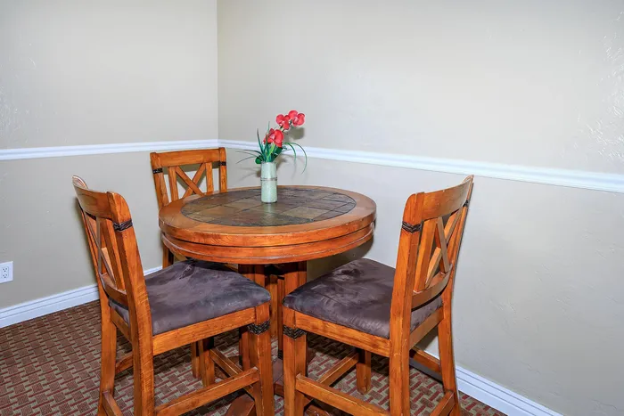 Cozy nook with a stylish round table and wooden chairs, accented by a vase of vibrant red flowers.