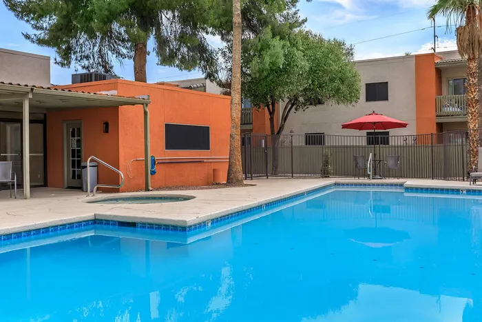 Inviting outdoor pool area with a vibrant orange building, shaded seating, and lush trees, perfect for relaxation and leisure.