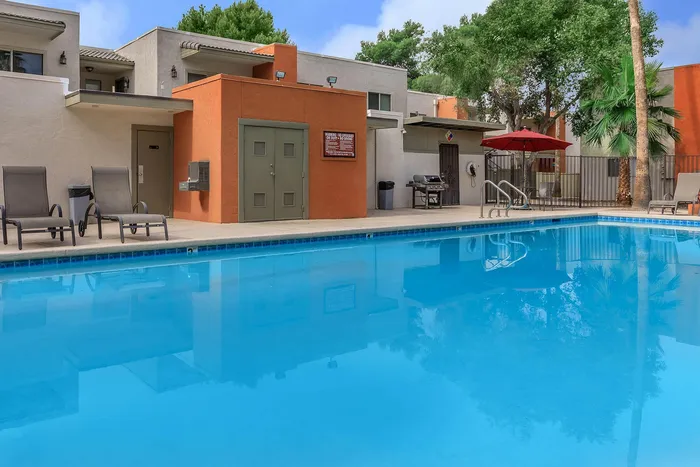 Inviting modern apartment complex with a sparkling blue swimming pool, comfortable lounge chairs, and lush greenery, offering a relaxing oasis in the heart of the community.