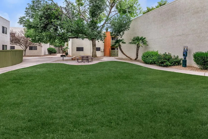 Charming courtyard with lush greenery, shaded picnic area, and contemporary apartment buildings, perfect for relaxation and community gatherings.