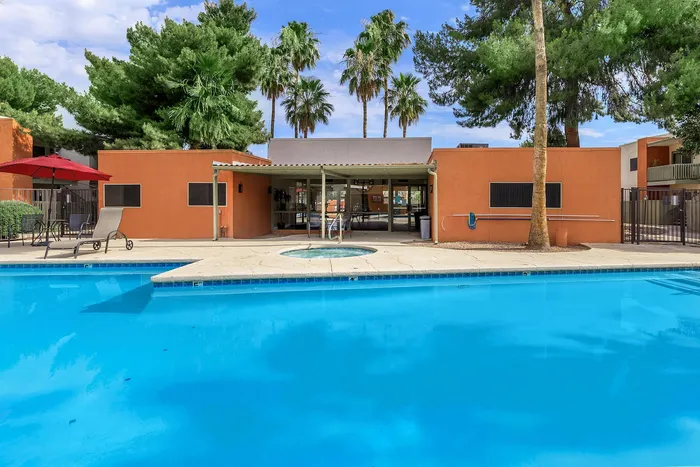 Inviting outdoor pool area with vibrant orange building, surrounded by lush palm trees and cozy lounging space.
