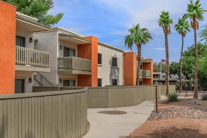 Charming apartment complex with vibrant orange accents, spacious balconies, and lush palm trees under a clear blue sky.