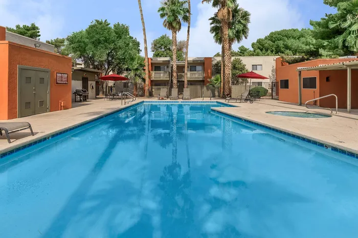 Inviting outdoor swimming pool area with lounge chairs and vibrant palm trees, perfect for relaxation and leisure in a modern apartment complex.
