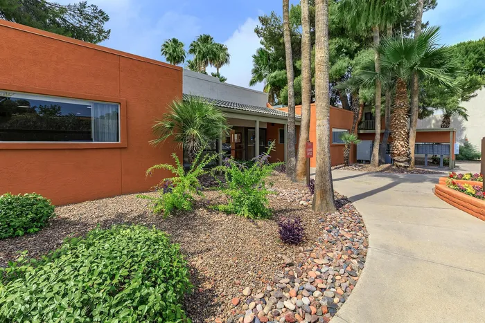 Charming apartment exterior with vibrant landscaping, palm trees, and inviting pathways in a sunny setting.
