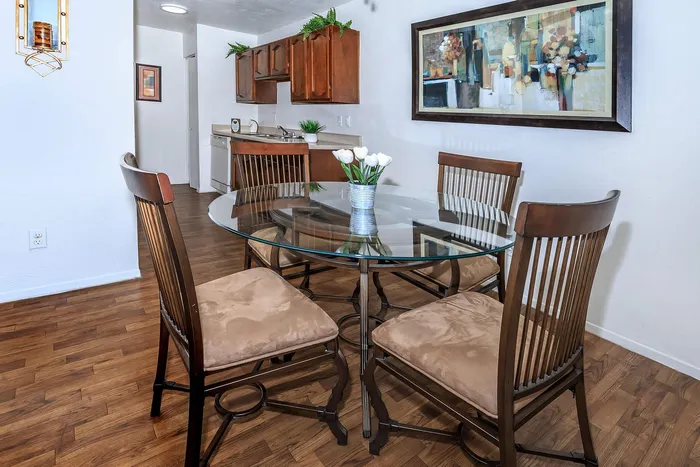 Inviting dining area featuring a stylish glass table, plush chairs, modern artwork, and warm wood cabinetry.