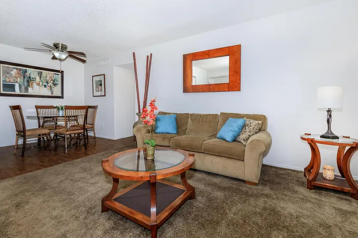 Inviting living room with cozy beige sofa adorned with colorful cushions, sleek glass coffee table, and chic dining area, ideal for entertaining in a modern apartment setting.