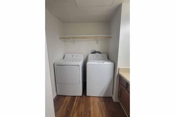 Convenient in-unit laundry featuring modern washer and dryer set in a cozy, well-lit nook with wooden flooring.
