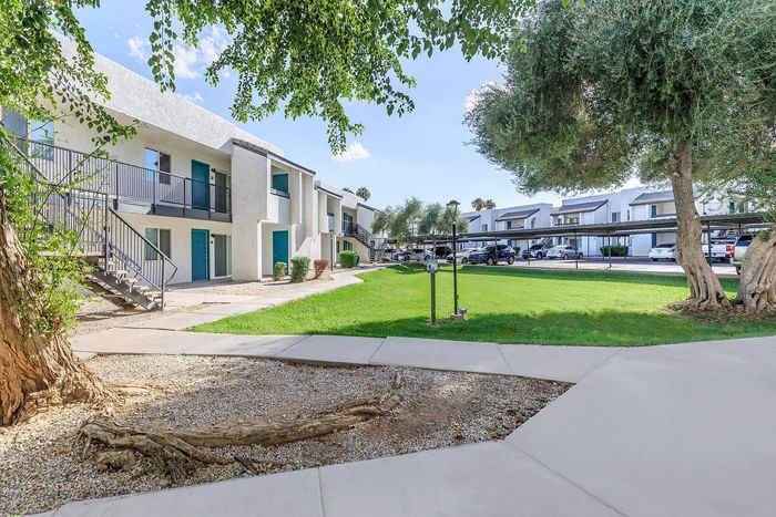 Charming apartment complex featuring modern architecture, lush green lawns, and inviting pathways under serene blue skies.