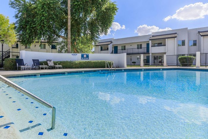 Luxurious apartment complex featuring a sparkling swimming pool with lounge chairs, surrounded by lush greenery and modern architecture.
