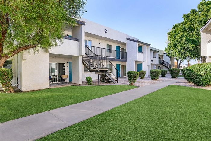 Charming two-story apartment building with private balconies, surrounded by lush green lawns and well-maintained landscaping.