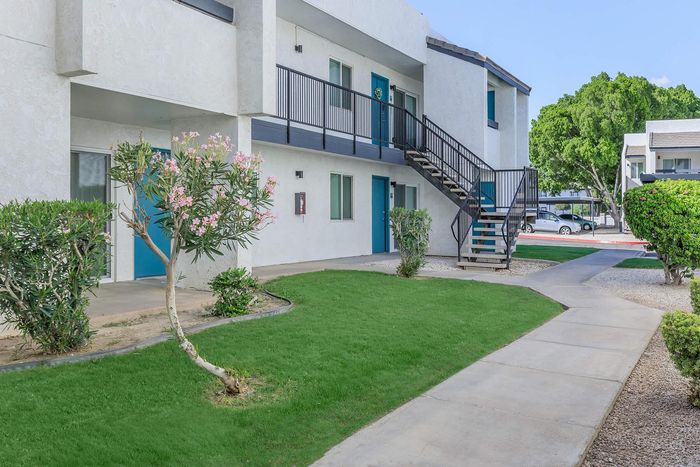 Charming apartment exterior with bright blue doors, lush landscaping, and inviting staircases in a serene community setting.