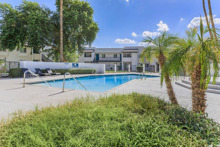 Relaxing apartment community with a sparkling pool, lush landscaping, and modern architecture under a clear blue sky.