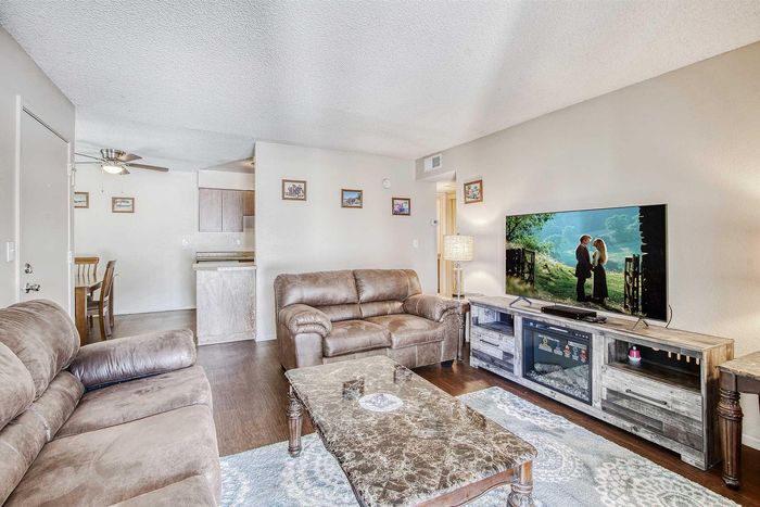 Inviting living room with plush leather sofas, elegant decor, and a flat-screen TV, leading into a cozy dining area and kitchen.