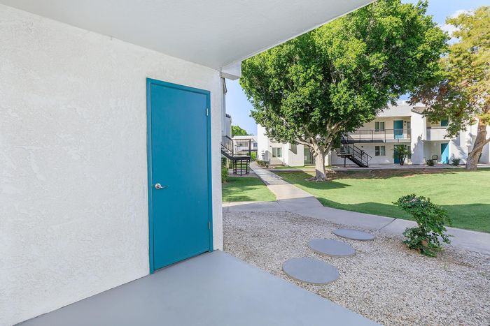 Inviting apartment exterior with stylish blue door, lush green lawn, and mature trees creating a serene atmosphere.