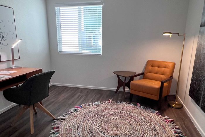 Inviting home office space featuring contemporary furniture with a stylish desk, modern chair, cozy leather armchair, and a chic floor lamp. Abundant natural light filters through the window, enhancing the serene ambiance and highlighting the elegant woven rug.