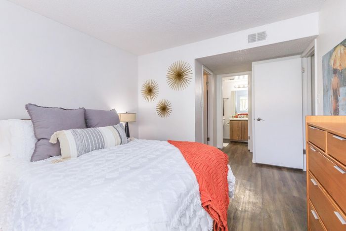 Bright and inviting bedroom featuring a cozy bed with plush pillows, elegant decor with gold accents, and access to a modern en-suite bathroom.