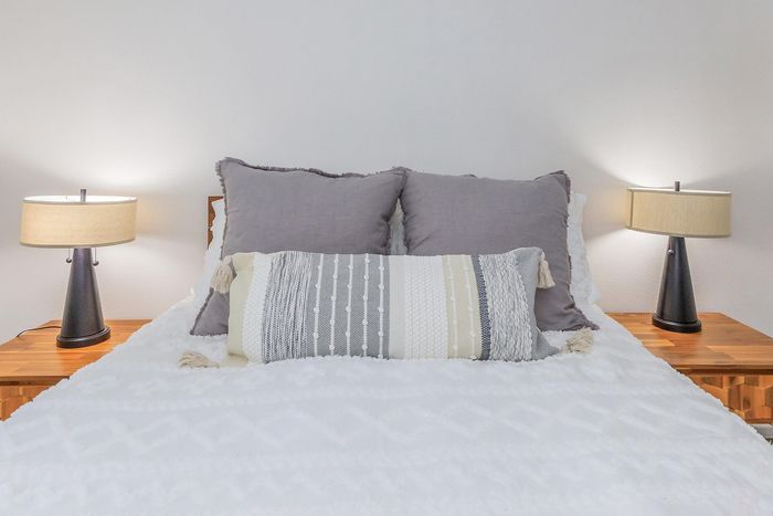 Cozy bedroom with plush pillows, elegant throw, and soft lighting from modern bedside lamps.