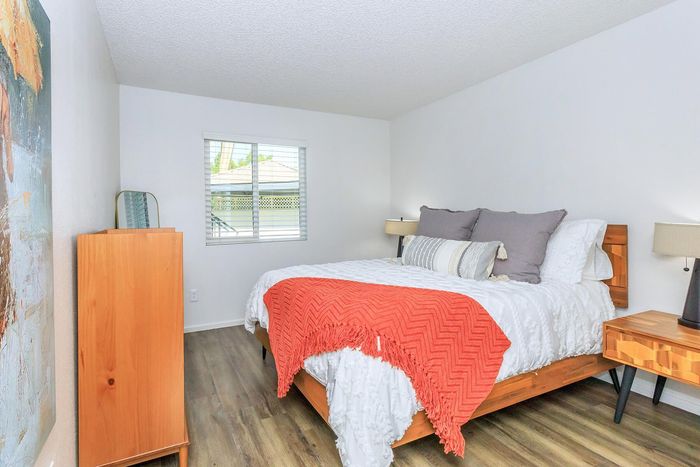 Inviting bedroom featuring a plush bed with vibrant orange accents, contemporary furniture, and ample natural light from a large window.