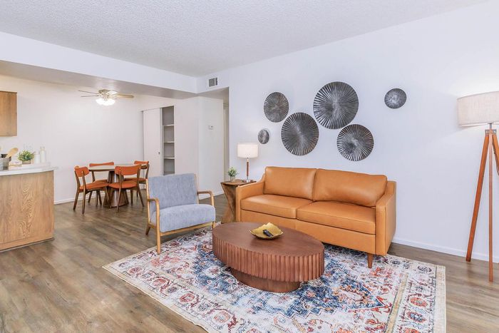 Inviting open-concept living room with a sleek leather sofa, cozy accent chair, and stylish wall art. Warm wooden flooring complements the modern decor, perfect for entertaining.