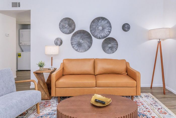 Chic modern living room with a sleek tan leather couch, stylish circular wall art, and elegant lighting, perfect for relaxation and aesthetics.