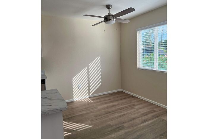 Bright and inviting room with sleek wooden flooring, large window, and a modern ceiling fan.