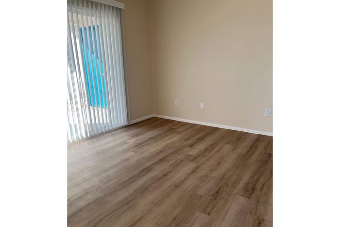Bright room with elegant wood flooring and sliding glass door featuring vertical blinds for natural light.