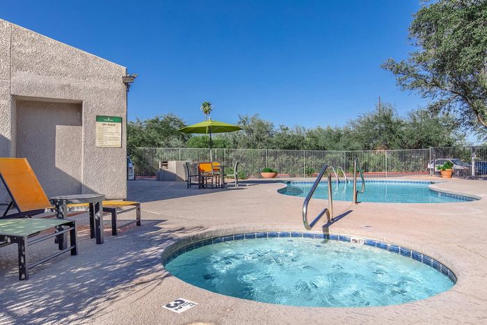 Inviting outdoor space featuring a sparkling pool and relaxing hot tub, surrounded by lush greenery and comfortable seating under a vibrant umbrella.