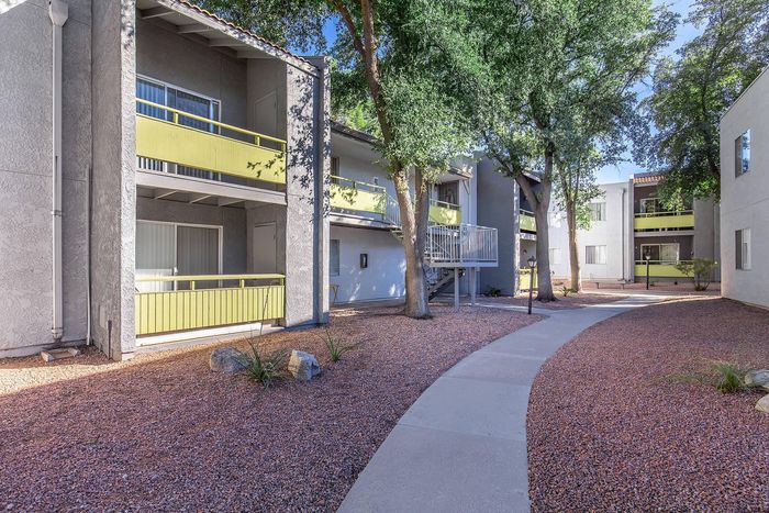 Charming apartment complex with modern balconies and lush trees under a bright blue sky.