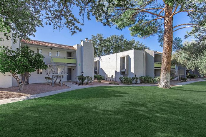 Serene apartment complex exterior featuring lush green lawns, mature trees, and modern architecture.