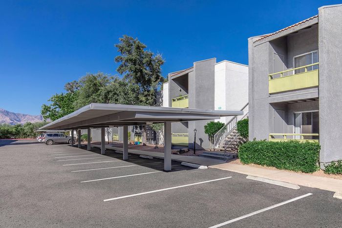 Charming apartment complex exterior with modern architecture, covered parking, lush greenery, and mountain views.
